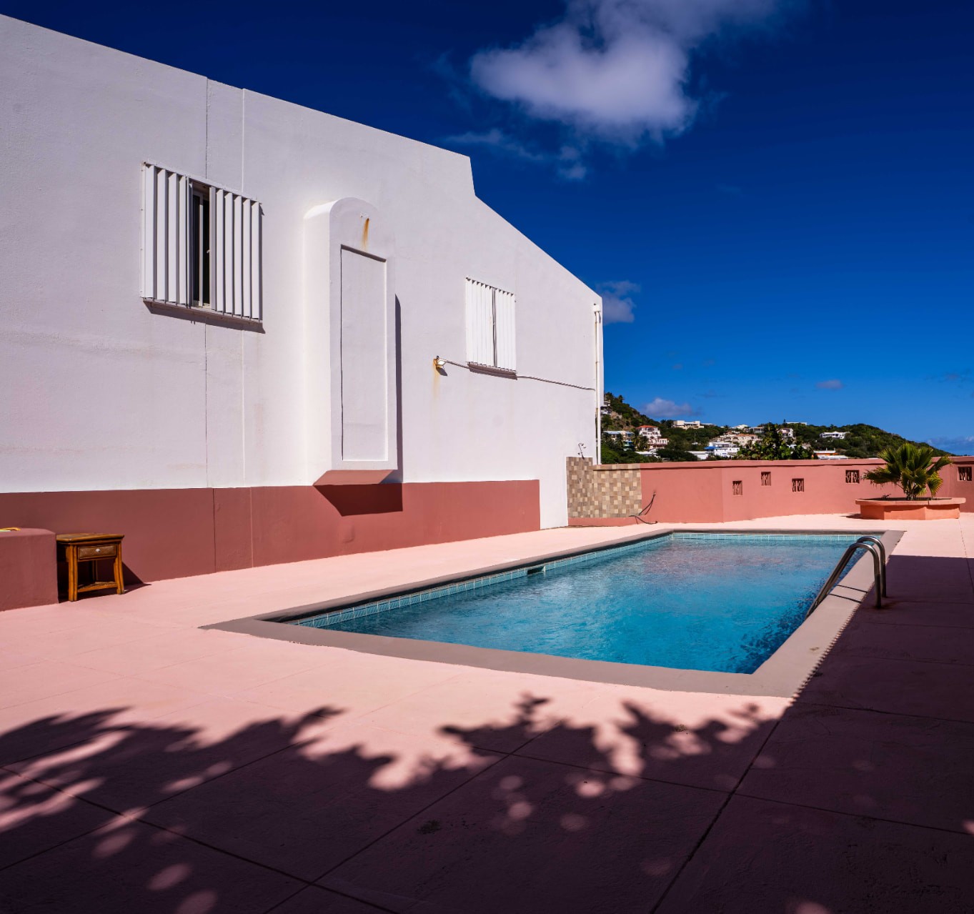 Pool terrace beside the white residence with hillside views